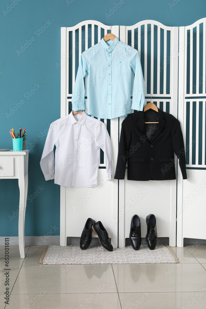 Stylish school uniform hanging on folding screen and shoes in room