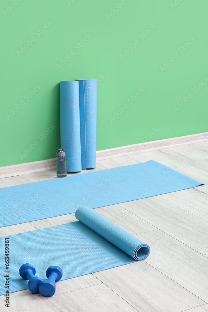 Yoga mats with dumbbells and bottle near green wall in gym