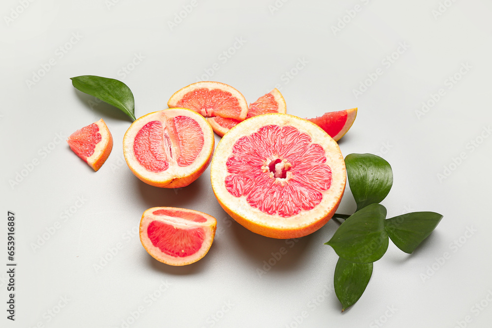 Composition with pieces of ripe grapefruit and plant leaves on light background
