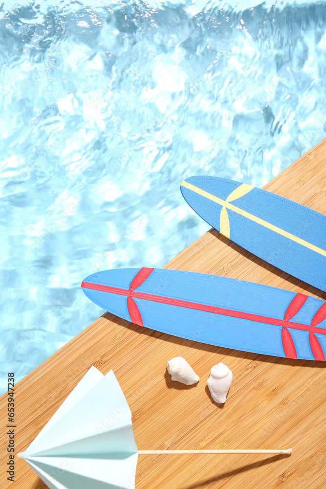 Composition with mini surfboards, umbrella and seashells on edge of swimming pool