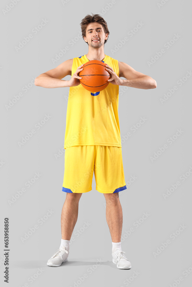 Portrait of young basketball player in yellow uniform holding ball on grey background