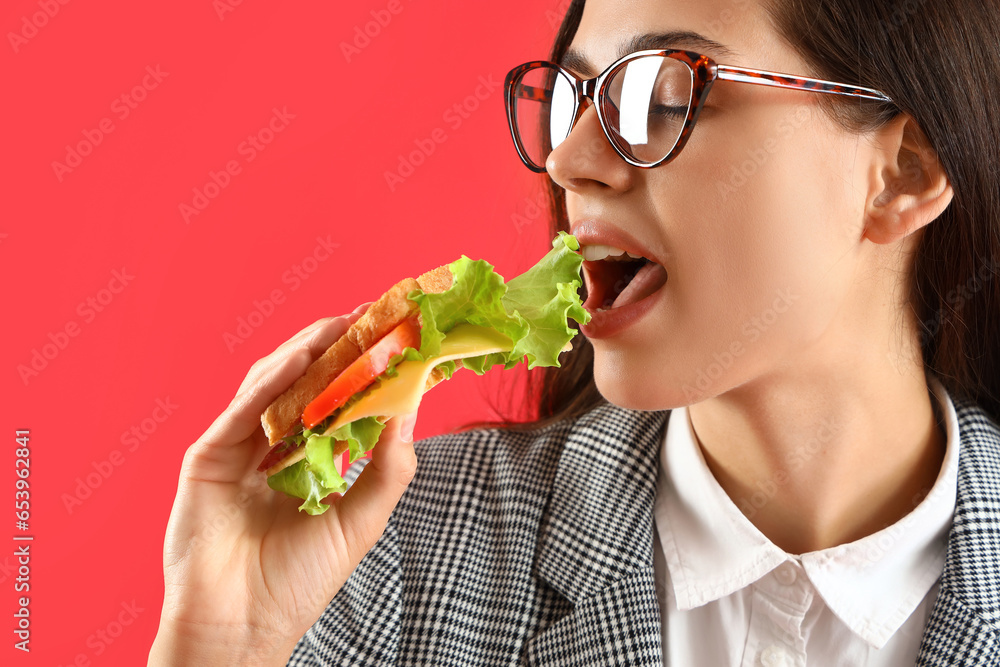 Young businesswoman eating tasty sandwich on red background, closeup