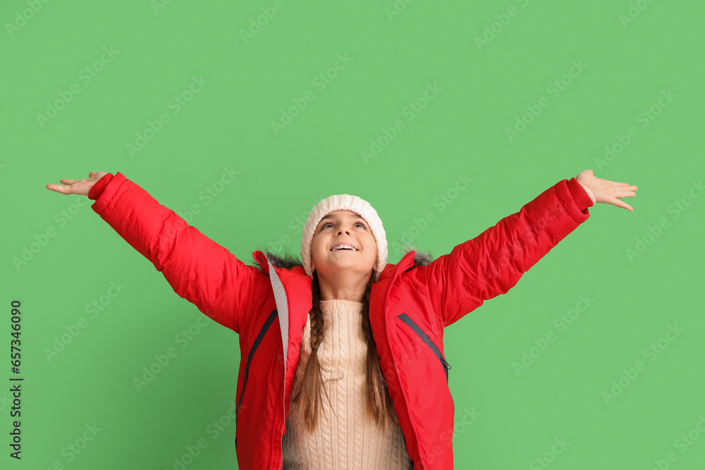 Happy little girl in hat and warm down jacket on green background