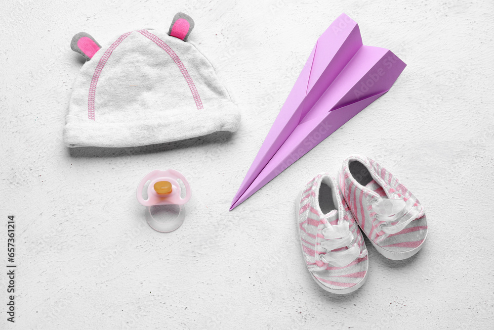 Baby hat, booties, pacifier and paper plane on light background