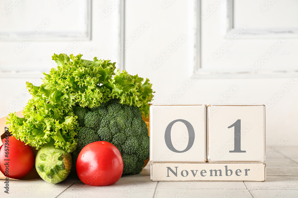 Fresh vegetables and cube calendar with date NOVEMBER 1 on table near white wooden wall. World Vegan Day concept