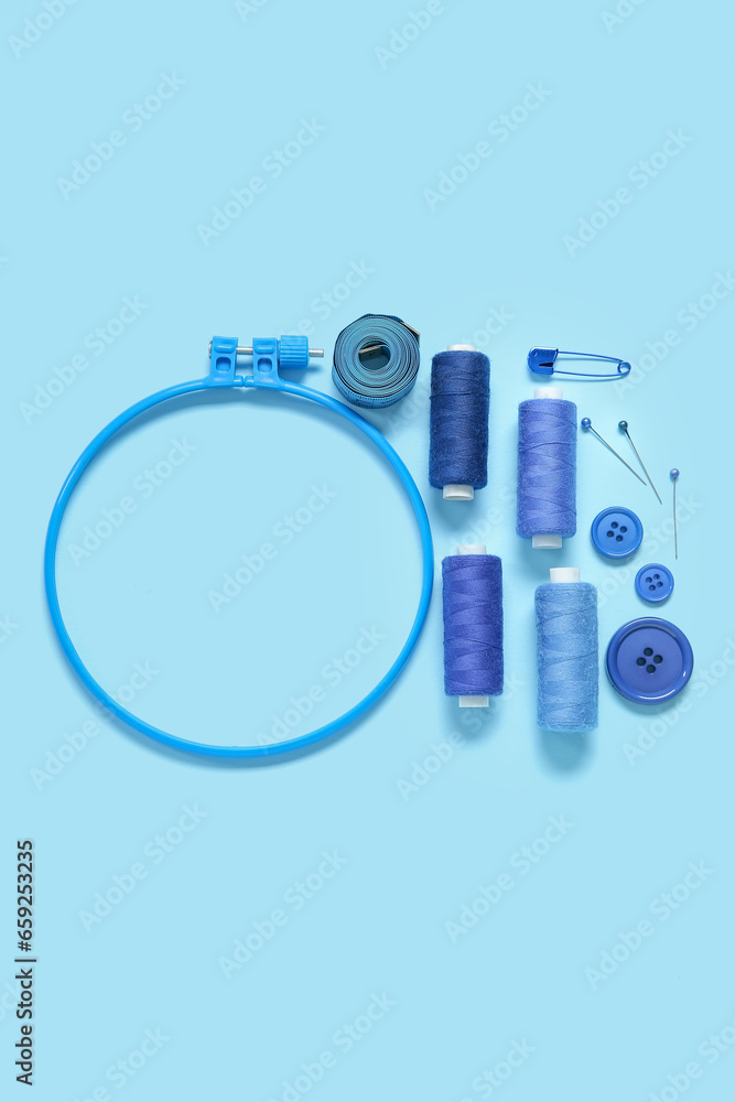 Embroidery hoop with thread spools, buttons and measuring tape on blue background