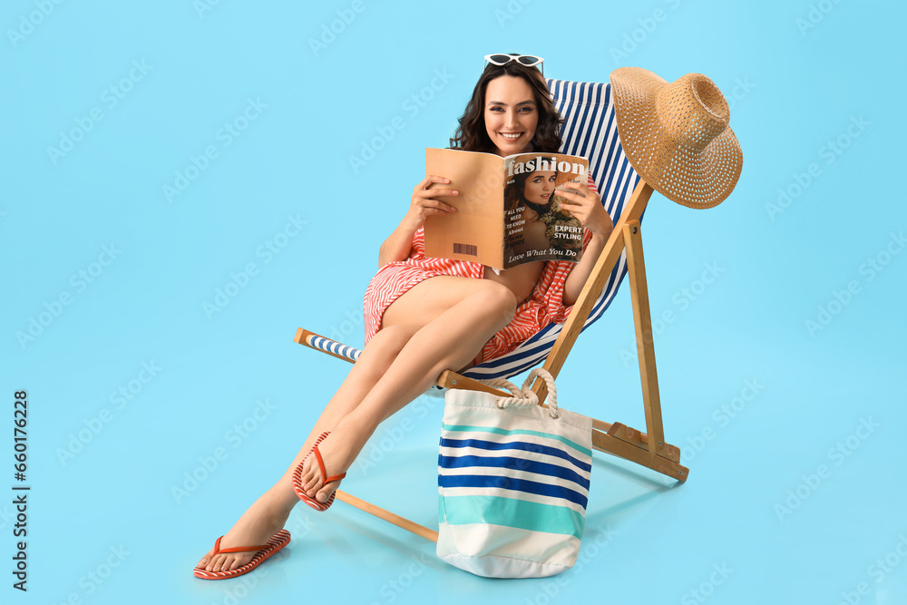 Young woman reading magazine in deck chair on blue background