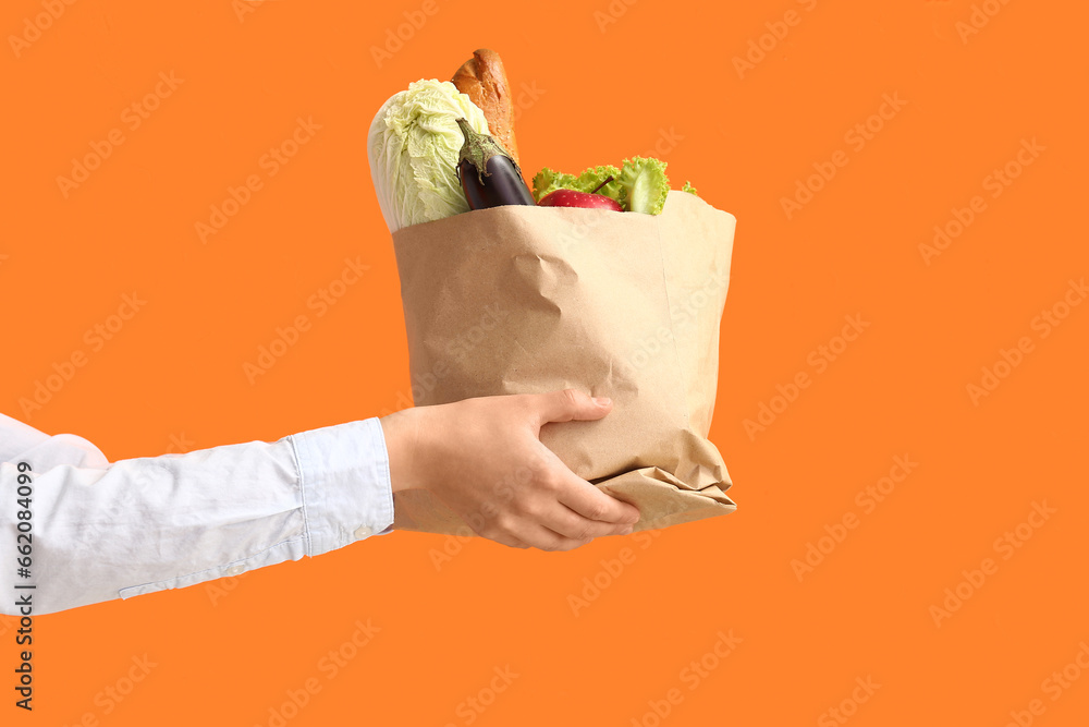 Woman holding paper bag with fresh food on orange background