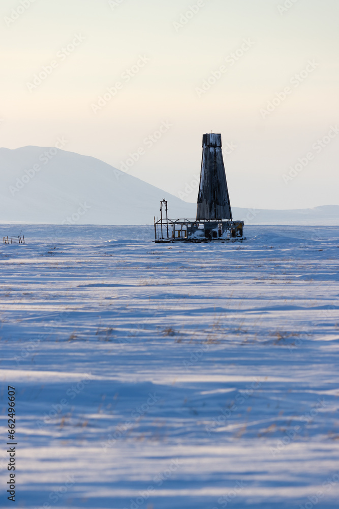 An old abandoned geological drilling rig in the snow-covered tundra. Winter Arctic landscape. Snow-capped mountains in the distance. Cold winter weather. Chukotka, Siberia, the Far North of Russia.