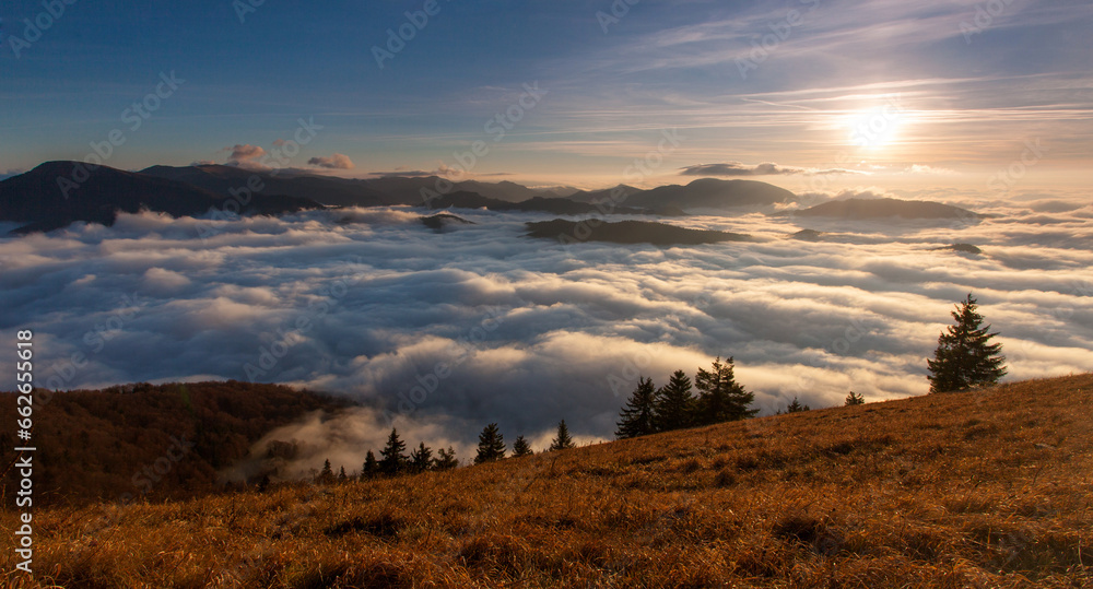 Sunset hidden behind clouds and fog over hills, bright yellow sun on colorful cloudscape, blue violet orange sky.