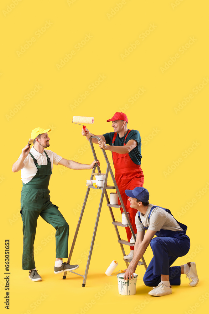 Team of male builders with paint cans on yellow background