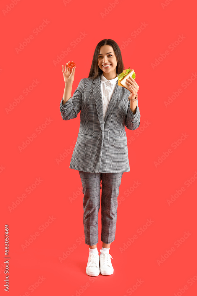 Young businesswoman with tasty sandwich on red background