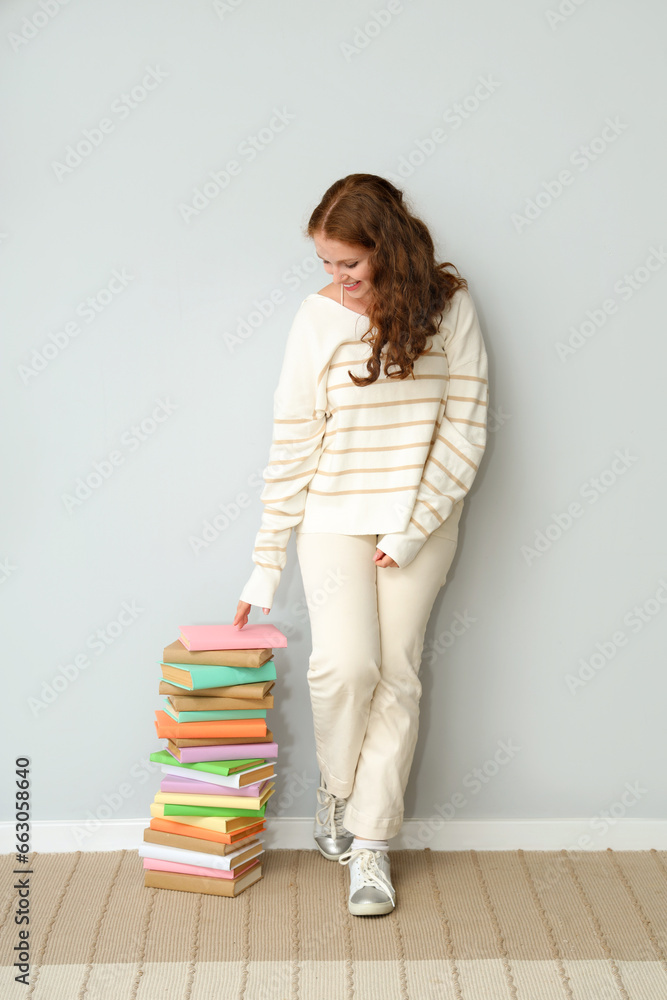 Young woman with stack of books near light wall