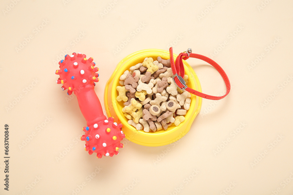 Bowl of dry pet food, rubber toy and collar on color background