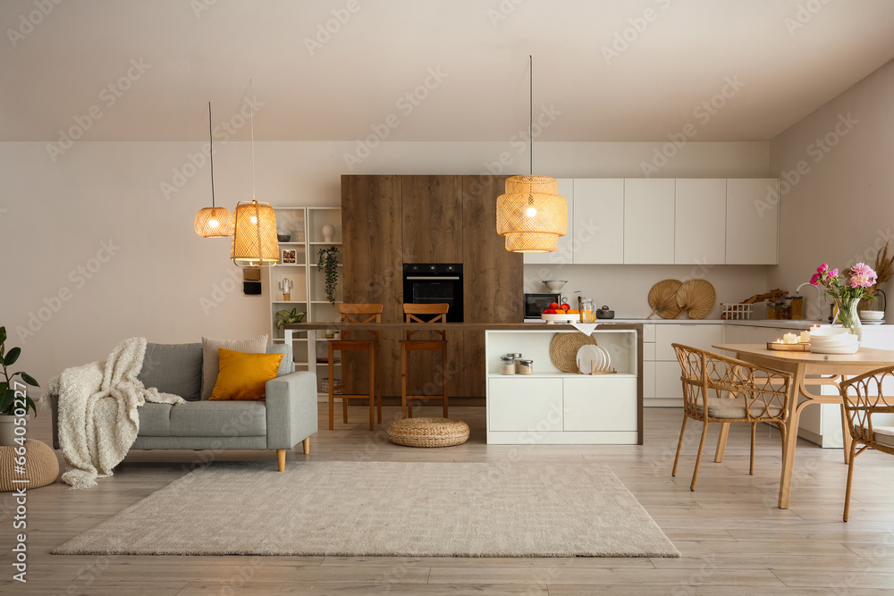 Interior of modern open plan kitchen with dining table, island, grey sofa and glowing lamps
