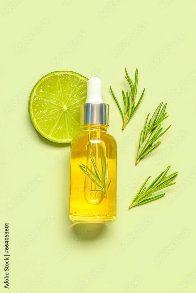 Bottle of citrus essential oil with herbs and lime on pale green background