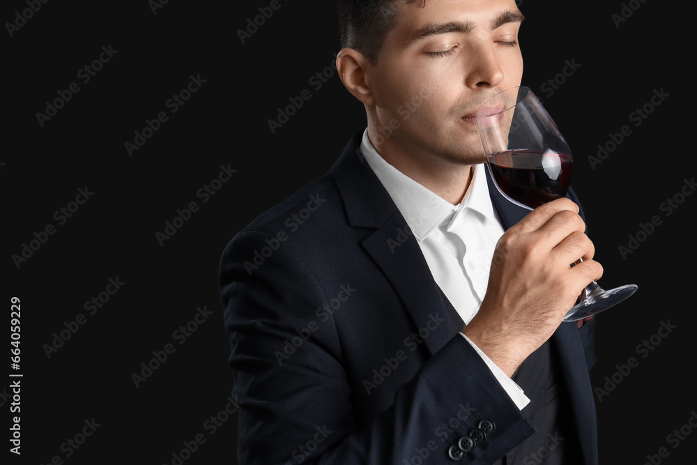 Young sommelier with glass of wine on black background, closeup