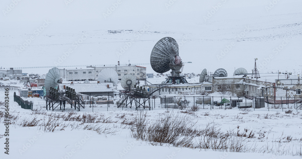 Large satellite dishes among the snow-covered tundra in the Arctic. Telecommunications infrastructure and communications in the Far North of Russia. Chukotka, Siberia. Winter industrial landscape.