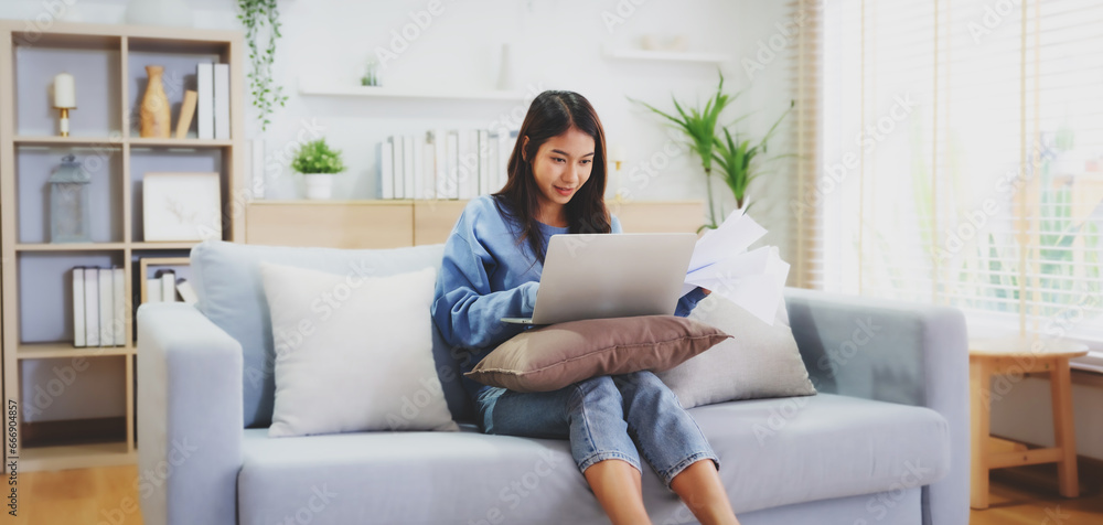 Young asian woman smile working on sofa in living room at home. Happy female using computer laptop and sitting on couch at house, Video call with friend