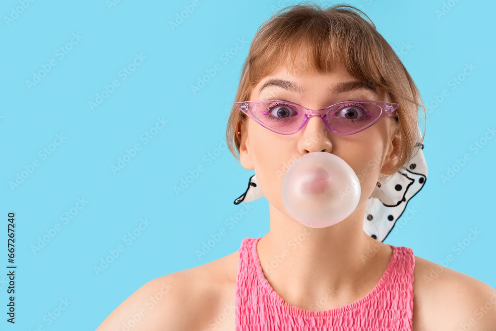 Beautiful young woman with chewing gum on blue background, closeup