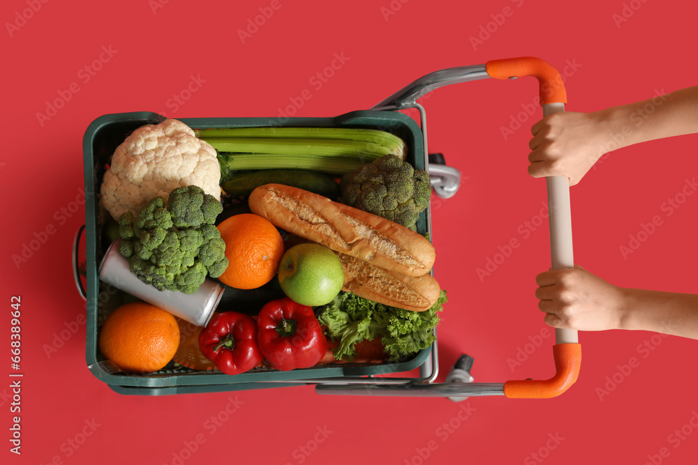 Woman pushing shopping cart full of food on red background