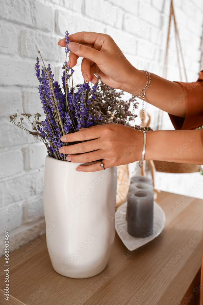 Beautiful young Asian woman with stylish bracelets and vase of lavender at home, closeup