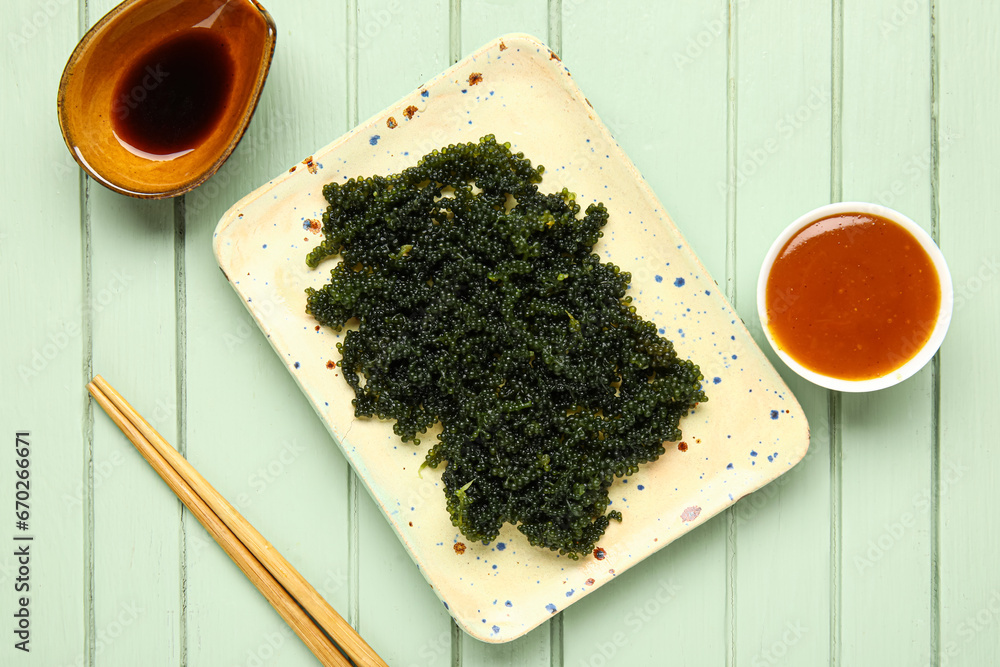 Plate with healthy seaweed, chopsticks and sauces on color wooden background