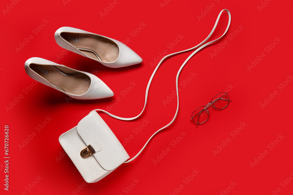 Stylish female shoes, handbag and eyeglasses on red background