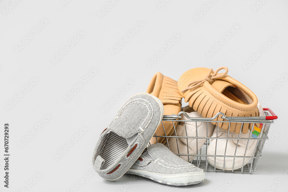 Shopping basket with different baby booties on grey background