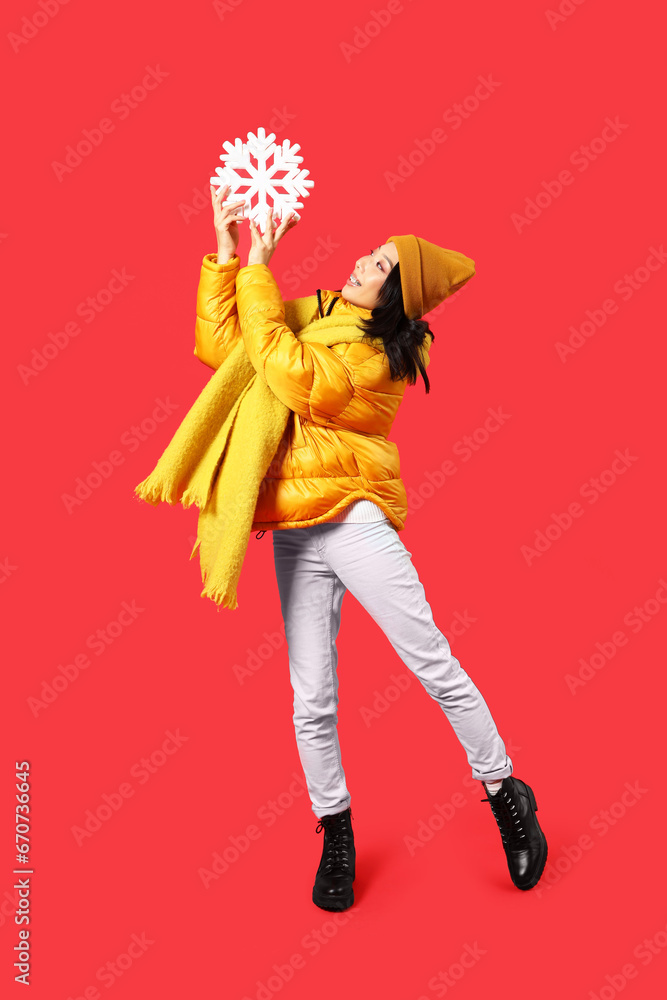 Young Asian woman in winter clothes with snowflake on red background