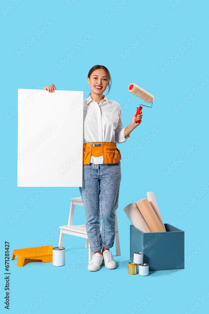 Female Asian decorator with paint roller and blank poster on blue background