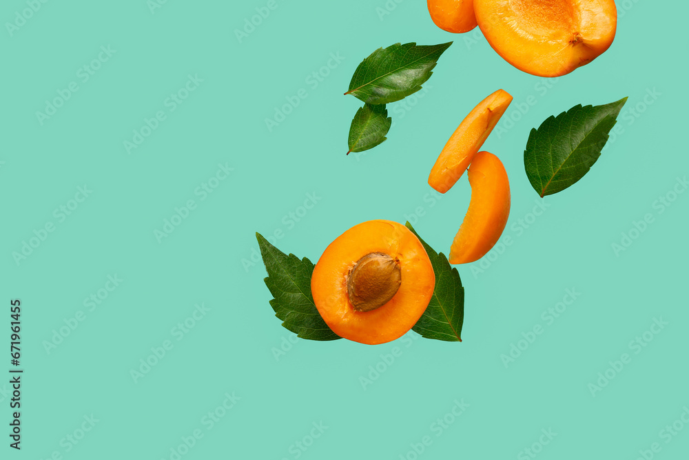 Flying halves of fresh apricot with pieces and leaves on turquoise background