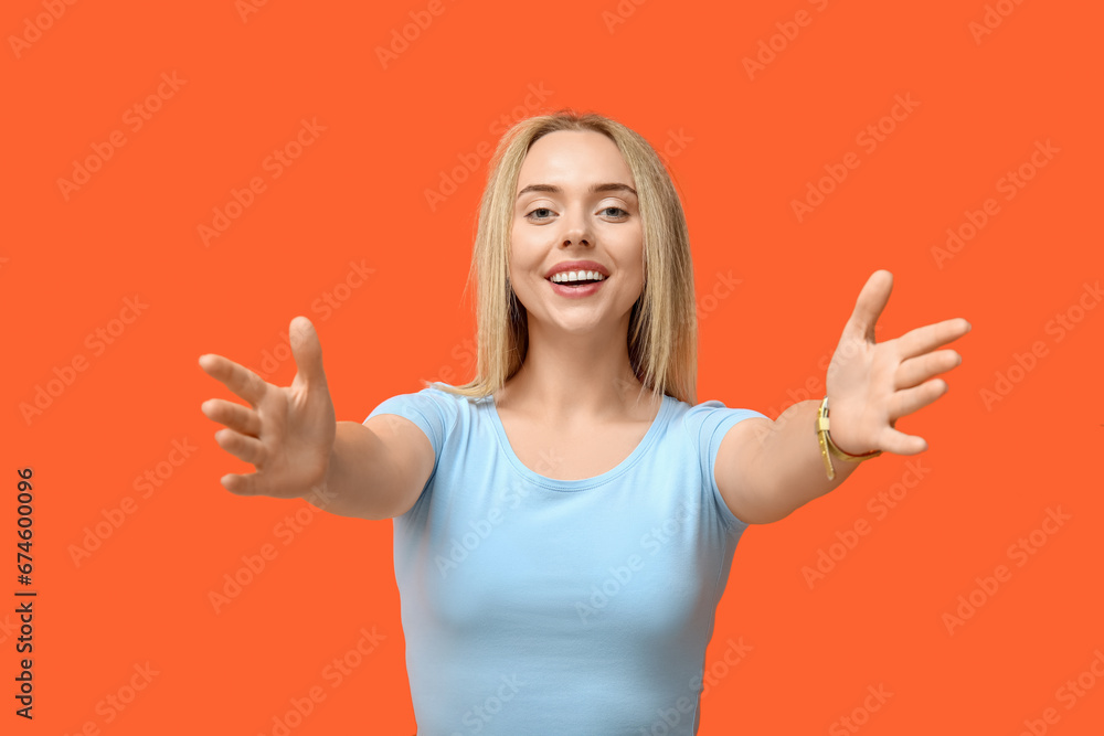 Young woman opening arms for hug on orange background