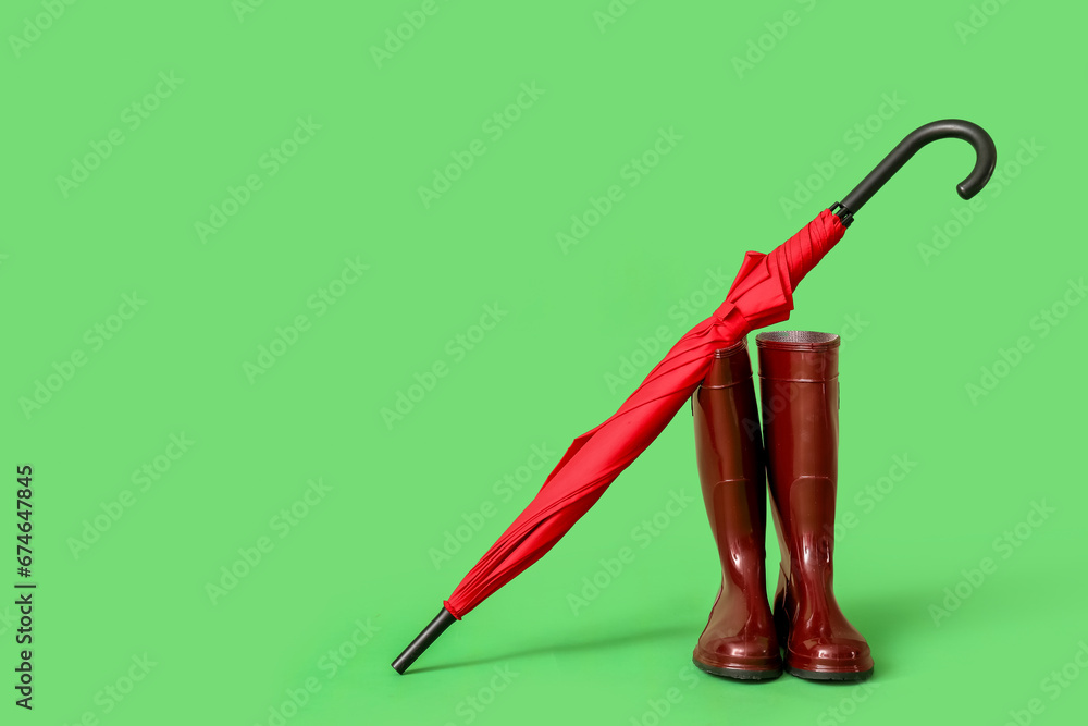 Red stylish umbrella and gumboots on green background