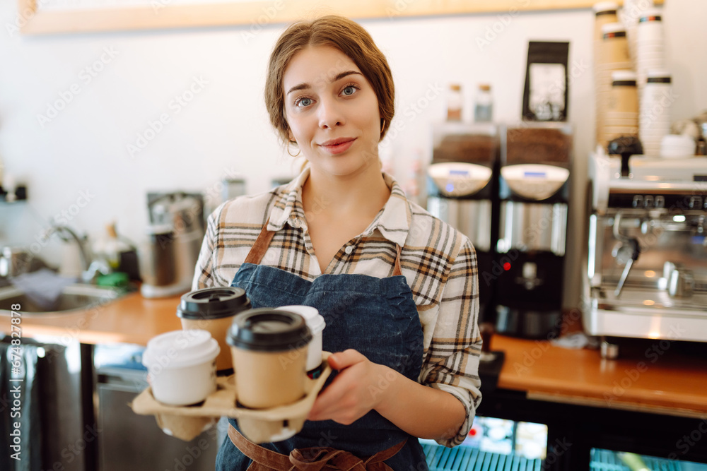 Female barista holding disposable takeaway cups. The young barista owner behind the bar gives out to-go orders. Business concept. Drinks to go.