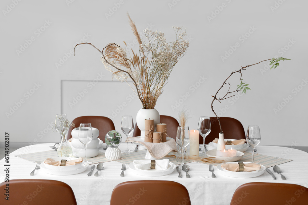 Elegant table setting with dried flowers, candles and plates at home