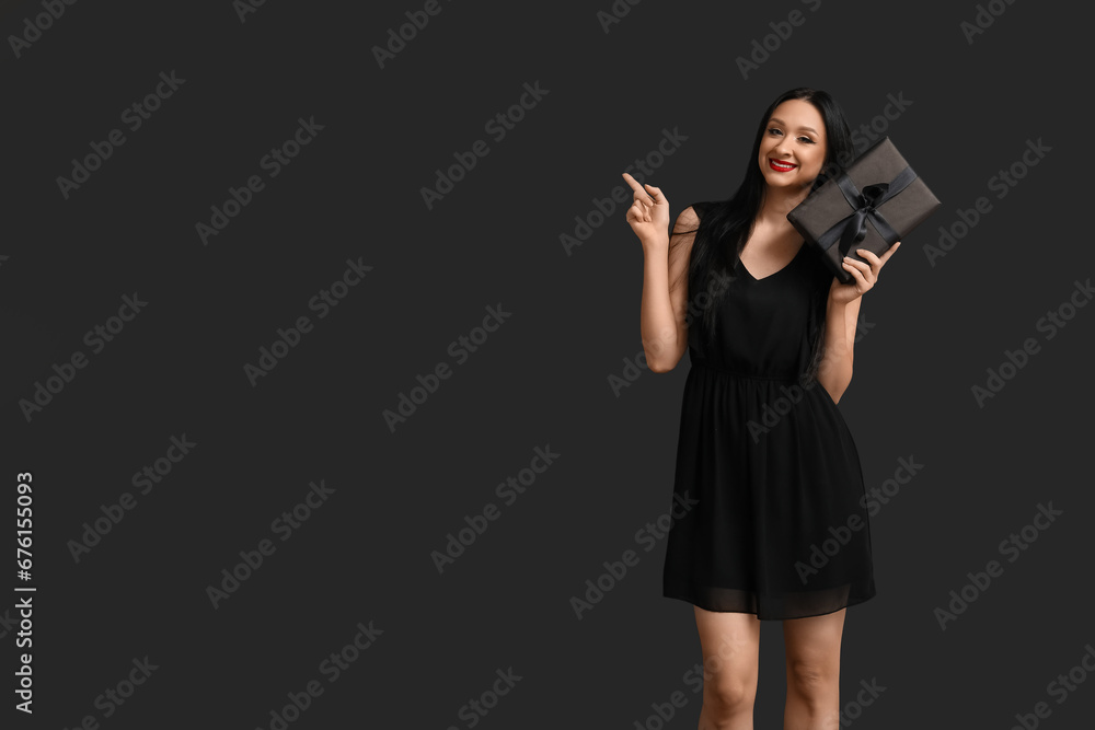 Beautiful happy woman with gift box pointing at something on dark background. Black Friday Sale