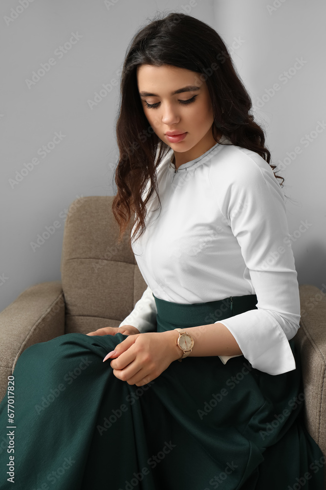 Beautiful young woman with wristwatch sitting on armchair in room