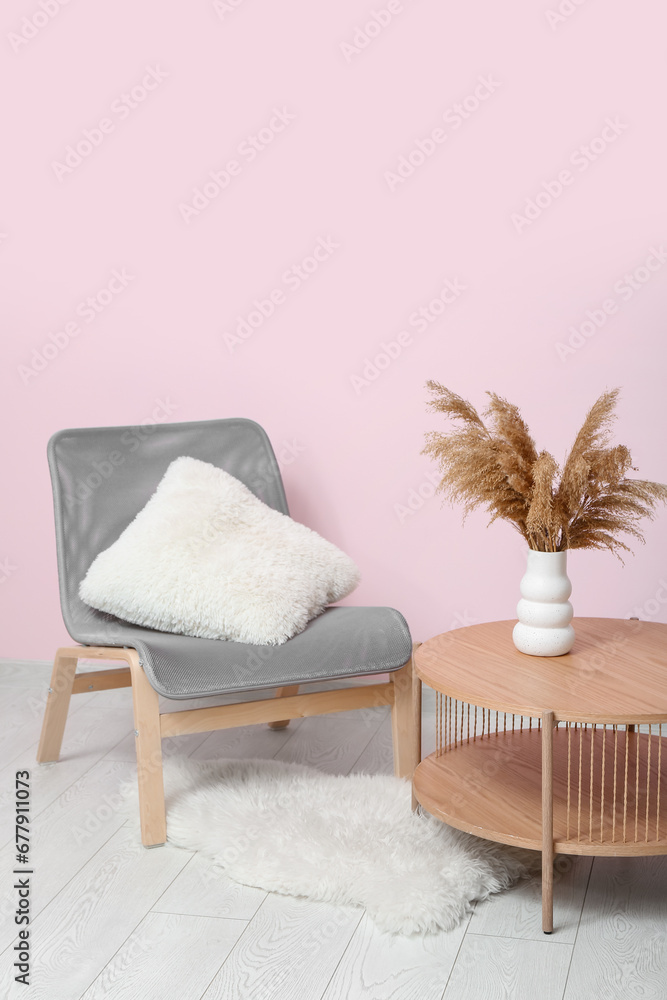 Comfortable armchair and wooden table with pampas grass near pink wall