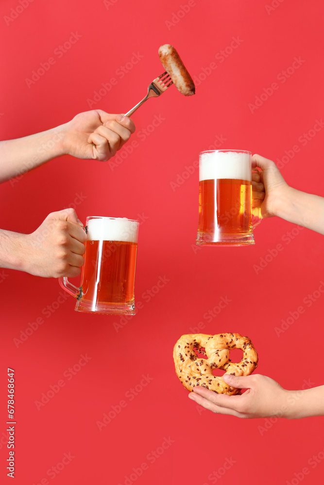 Many hands with mugs of cold beer, sausage and pretzel on red background