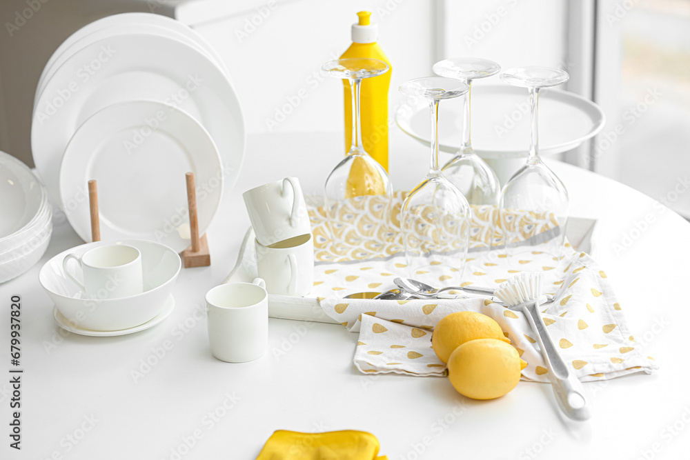 Set of white dishes with cleaning supplies and lemons on table in kitchen