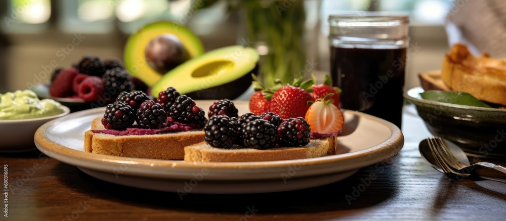 In the background of the kitchen, a white plate was laid out with a healthy breakfast spread whole wheat bread with a blackberry jam, ripe banana slices, and avocado spread, all packed with natural