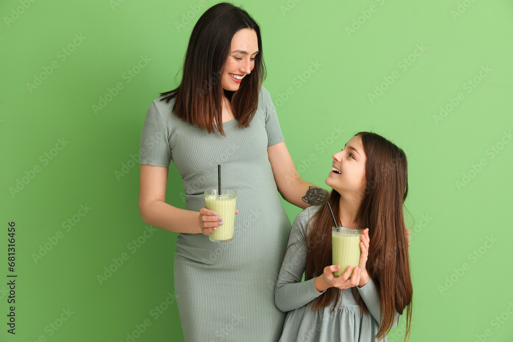 Little girl with her pregnant mother drinking smoothie on green background