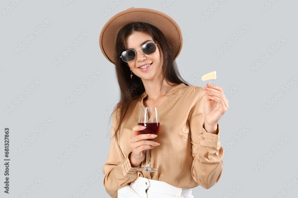 Beautiful young woman with glass of wine and cheese on light background
