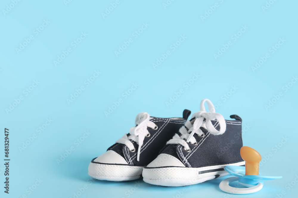 Stylish baby shoes with pacifier on blue background