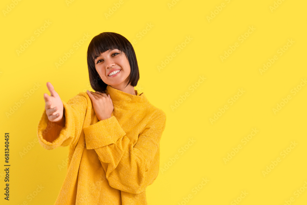 Young woman opening arms for hug on yellow background